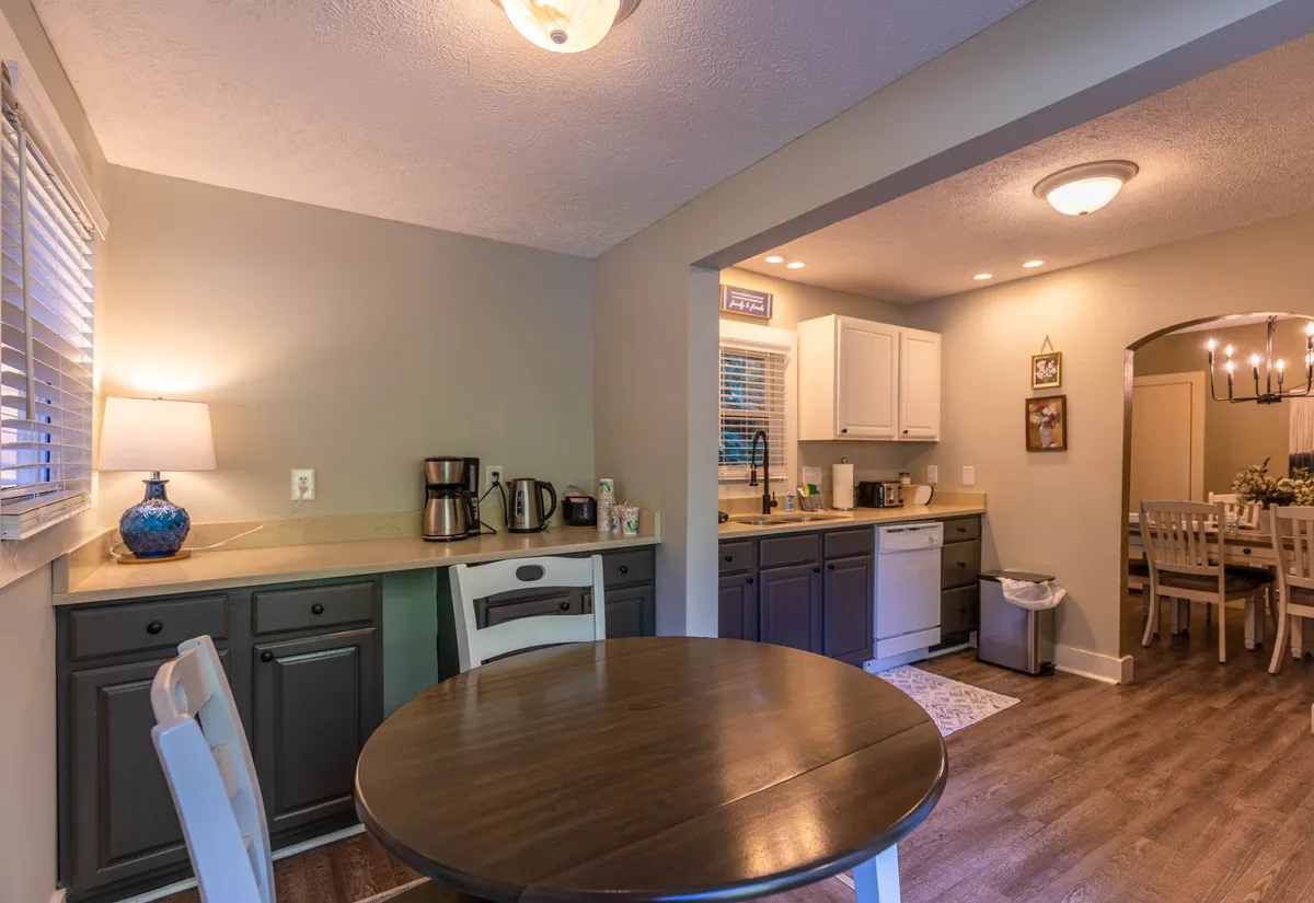 A warm, open kitchen and dining area, highlighting a central dining table, kitchen counter, and appliances, with gentle lighting that creates a welcoming atmosphere. The scene evokes the comfort and camaraderie of shared meals and relaxed mornings, tying into the theme of unwinding after exploration.