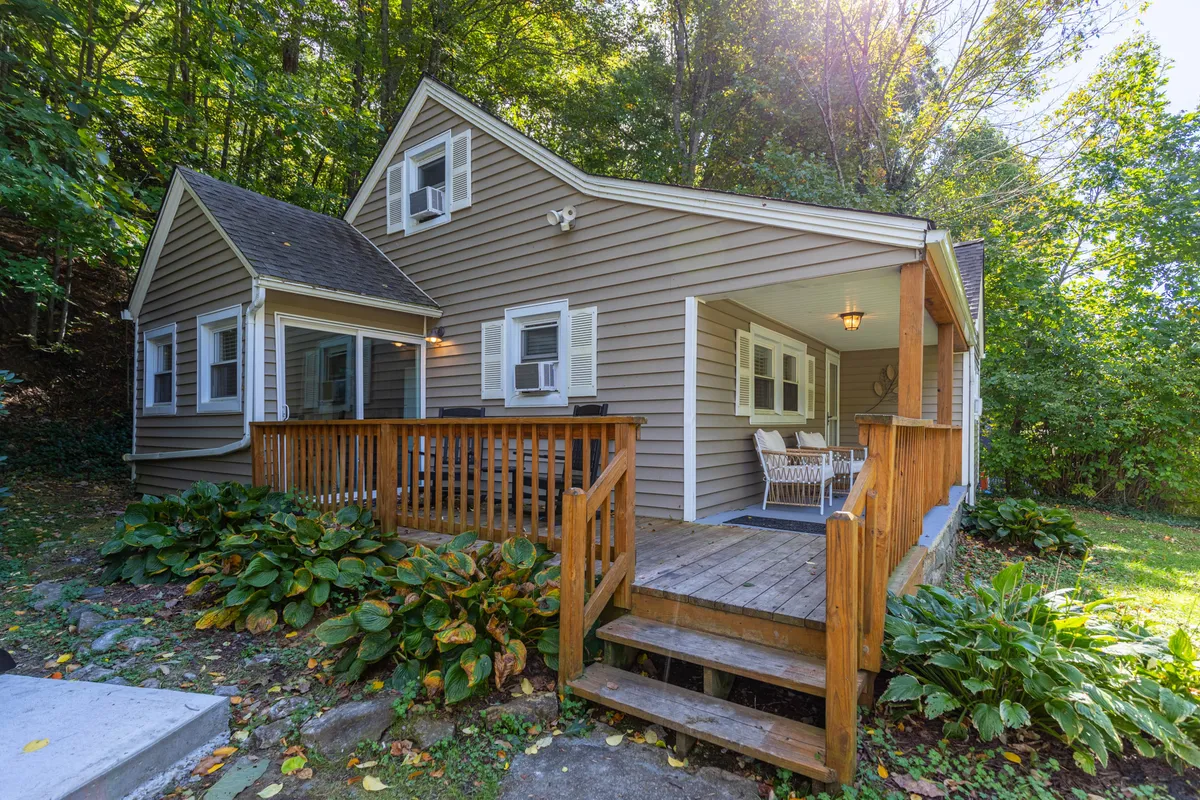 The image showcases the inviting front porch of Hot Toddy Cottage, framed by a classic wooden railing and surrounded by a charming, landscaped garden. The scene radiates warmth and tranquility, suggesting a perfect spot to relax with morning coffee or unwind in the evening, all set in the peaceful town of Banner Elk.