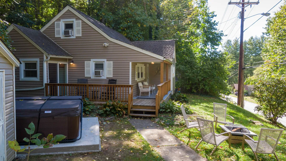 A close-up of the wooden deck area featuring an inviting hot tub and comfortable outdoor seating, surrounded by natural greenery. The deck feels intimate and is staged for relaxation and socializing.