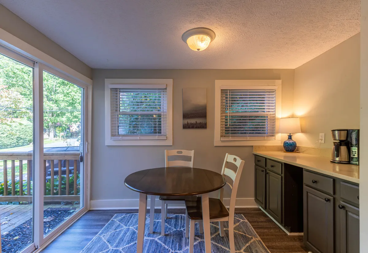 A cozy breakfast nook with a round table, a blue lamp providing soft illumination, a coffee maker ready for early mornings, and framed artwork adding a touch of personality. Sunlight streams in, enhancing the inviting mood.