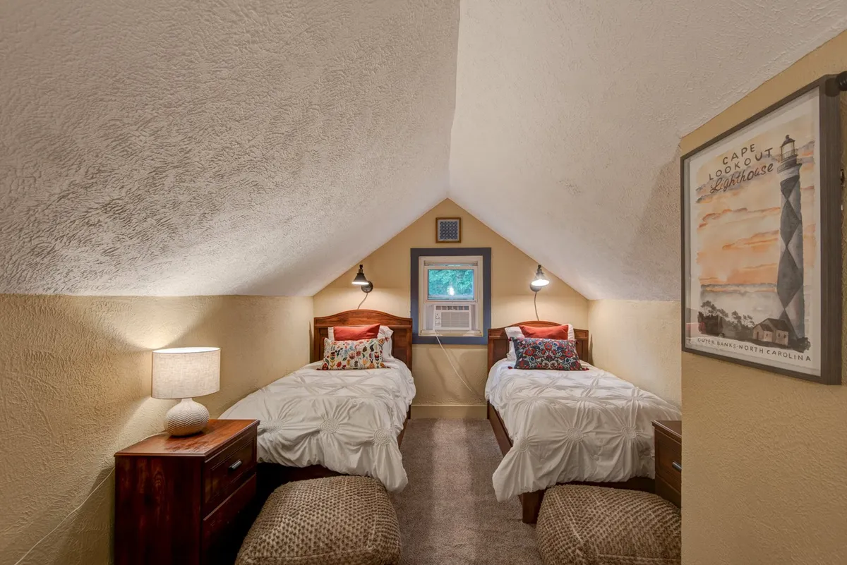 A playful twin bedroom featuring two twin beds with decorative pillows, wall-mounted reading lamps, a cheerful lighthouse poster, and a window offering a bright view. The design is both whimsical and kid-friendly, ideal for sleepovers or bedtime stories.
