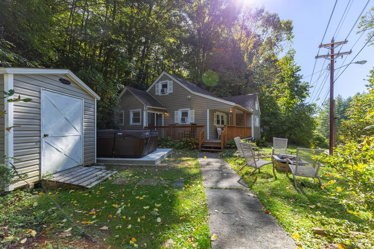 A wide view of the home's backyard shows a fully fenced area with a visible hot tub, outdoor seating, a shed, and plenty of open lawn space. The fence is clearly visible in the background, and the outdoor setup emphasizes both relaxation and play possibilities.