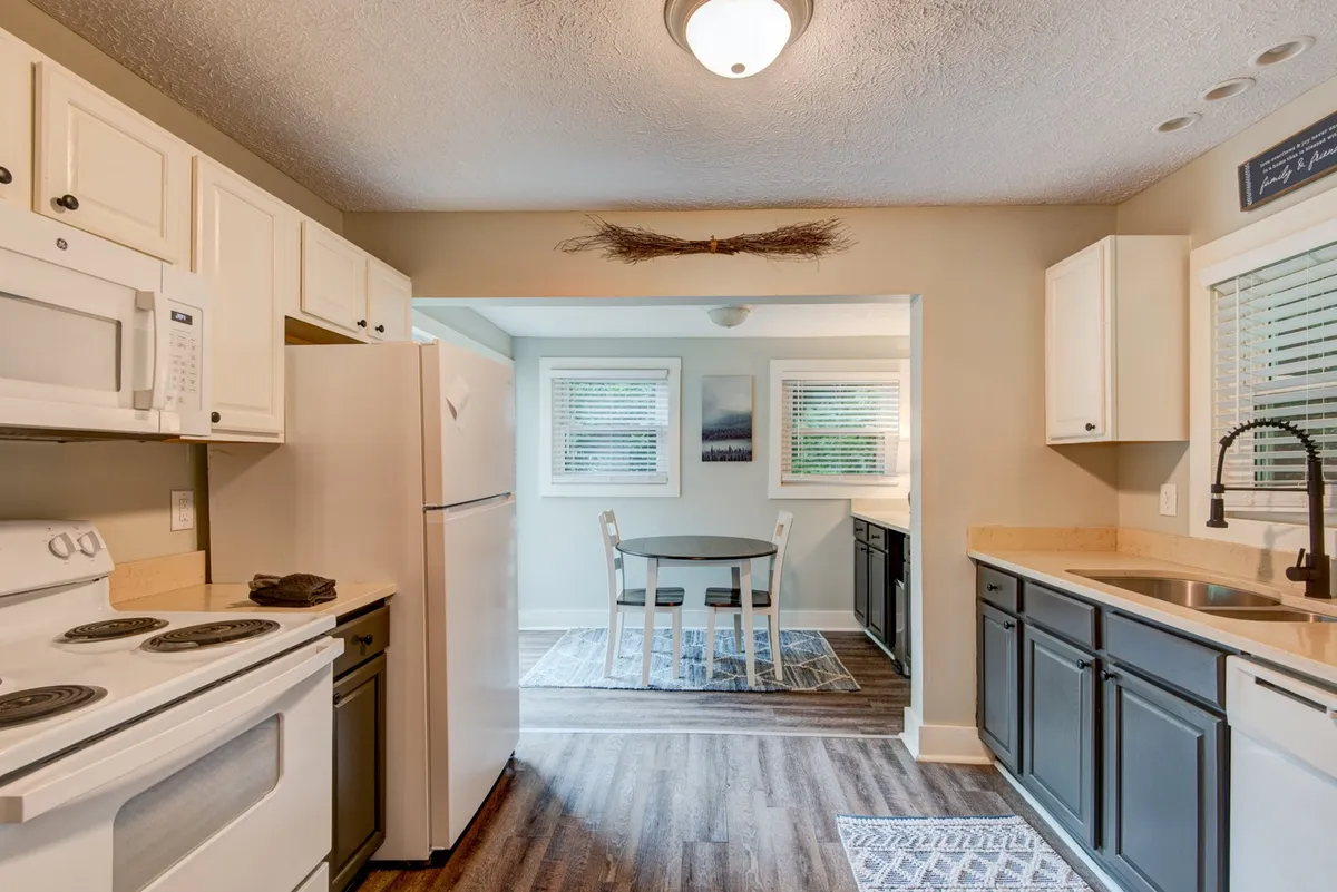A spacious, well-lit kitchen featuring modern appliances, a central dining table set for a family meal, and charming decorative touches like a broom in the corner. The room exudes warmth and welcomes culinary activity, suggesting both everyday use and special gatherings.