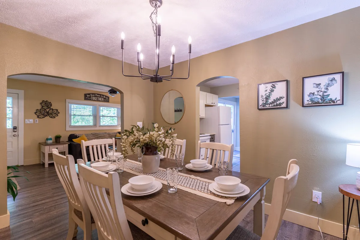 A warmly lit dining area features a wooden table, elegant chandelier, a floral centerpiece, and wall art, evoking a sense of celebration and intimacy.