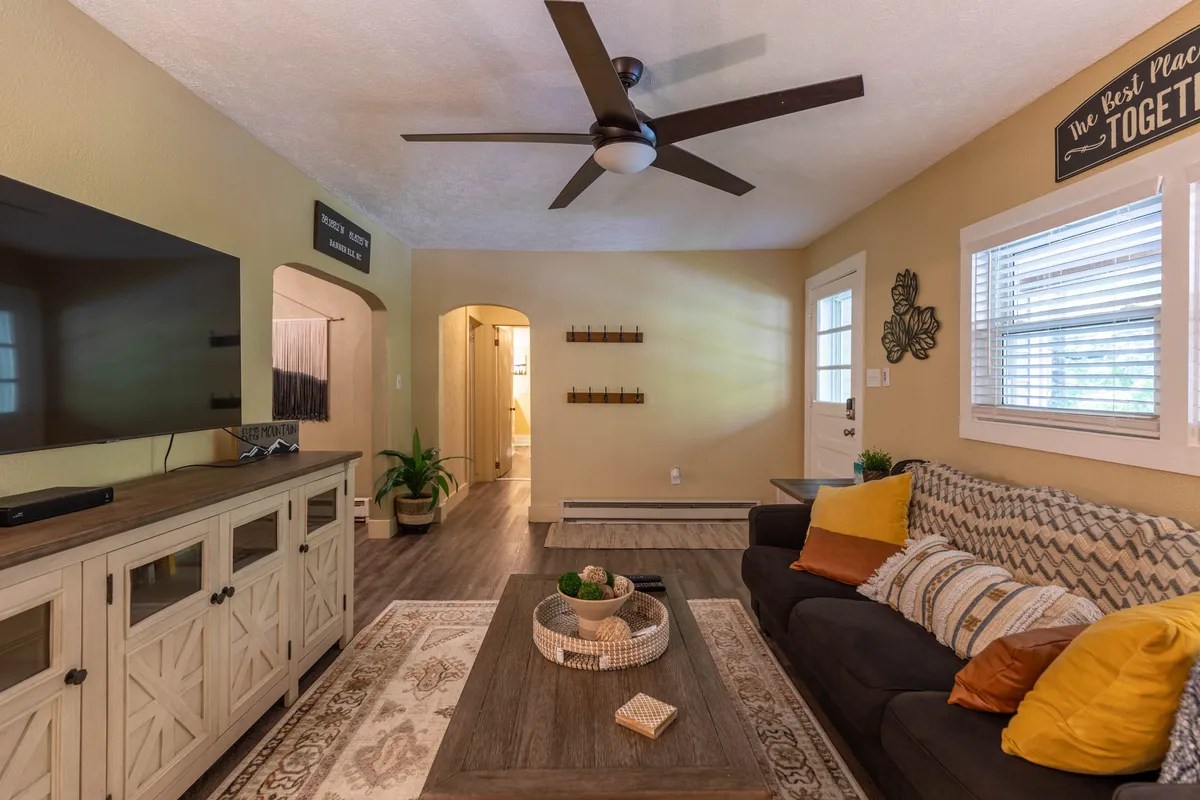 This image showcases a cozy living area with a comfortable sofa, a coffee table, and a television. The scene invites relaxed gatherings, with natural light filtering through the windows and a welcoming, homey atmosphere.