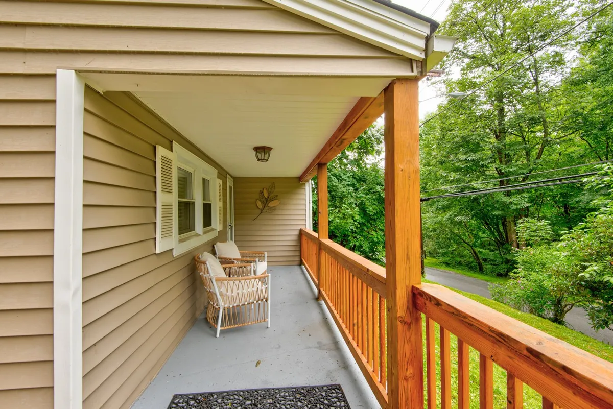 The image captures a charming exterior view of the cottage’s front porch, featuring a cozy porch swing surrounded by lush greenery and bordered by a wooden railing. The space feels peaceful and inviting, offering a spot to relax and enjoy the outdoors—perfect for unwinding with your pet after a day of exploring.