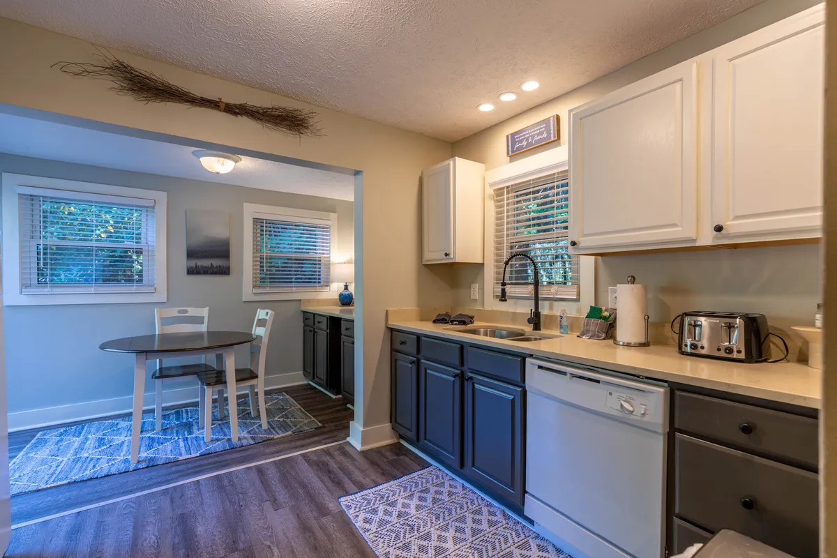 An open kitchen and dining area with plenty of natural light from large windows, classic kitchen cabinetry, a sink, and a dining table that encourages lingering conversations over coffee or brunch. The inviting mood hints at both everyday and special occasions.