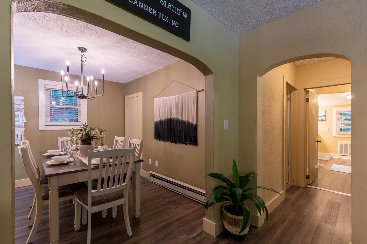 A warm dining area is centered around a dining table beneath a glowing chandelier, with a wall hanging and a lush plant adding personality and vibrancy to the space.